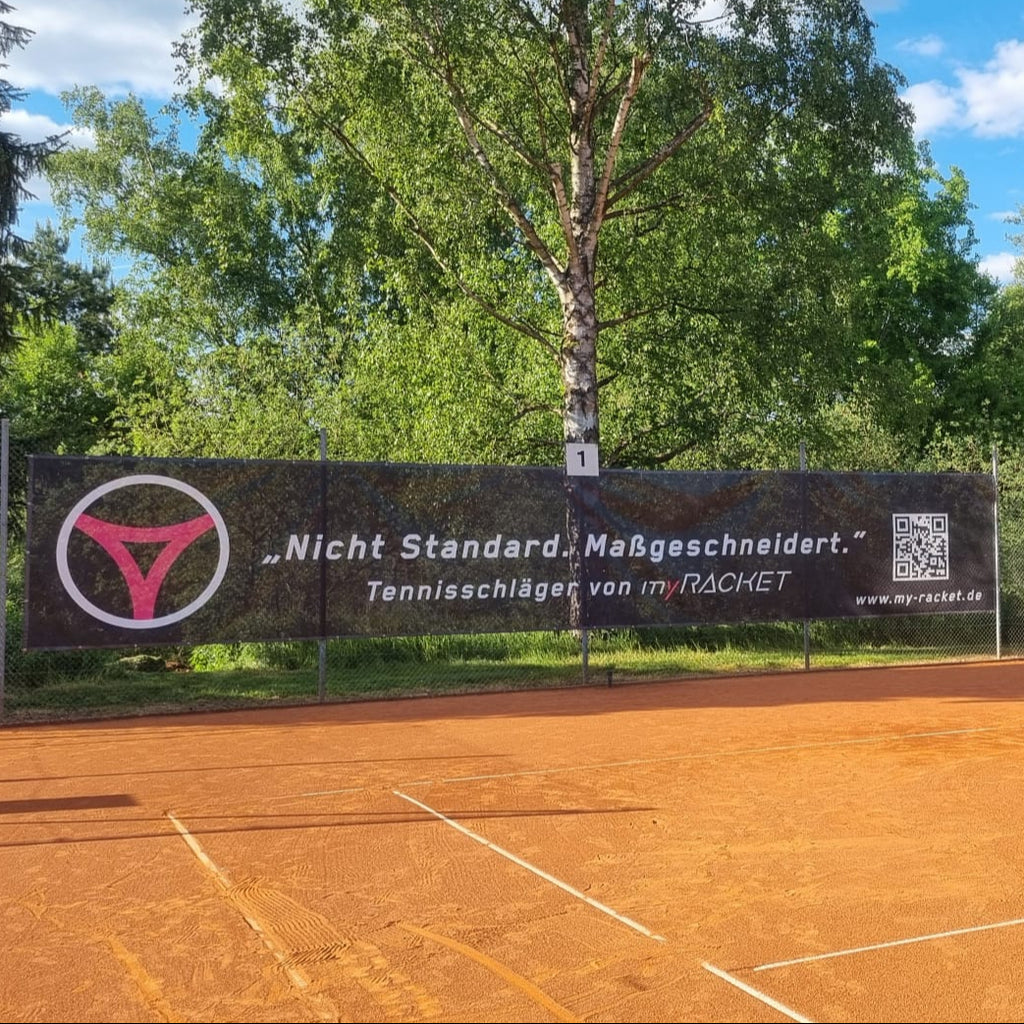 Schwarzer myRacket Windfänger mit Slogan am Zaun eines Sandplatzes – Gesamtansicht