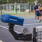 Cámara Baseline Vision con soporte en el poste de la red y, al fondo, dos jugadores en la pista