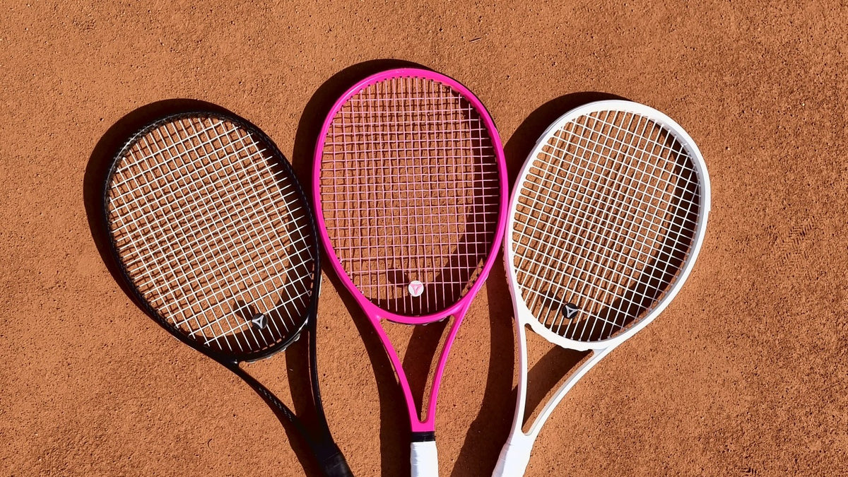 Tres raquetas de tenis myRacket en negro, rosa y blanco en abanico sobre tierra batida
