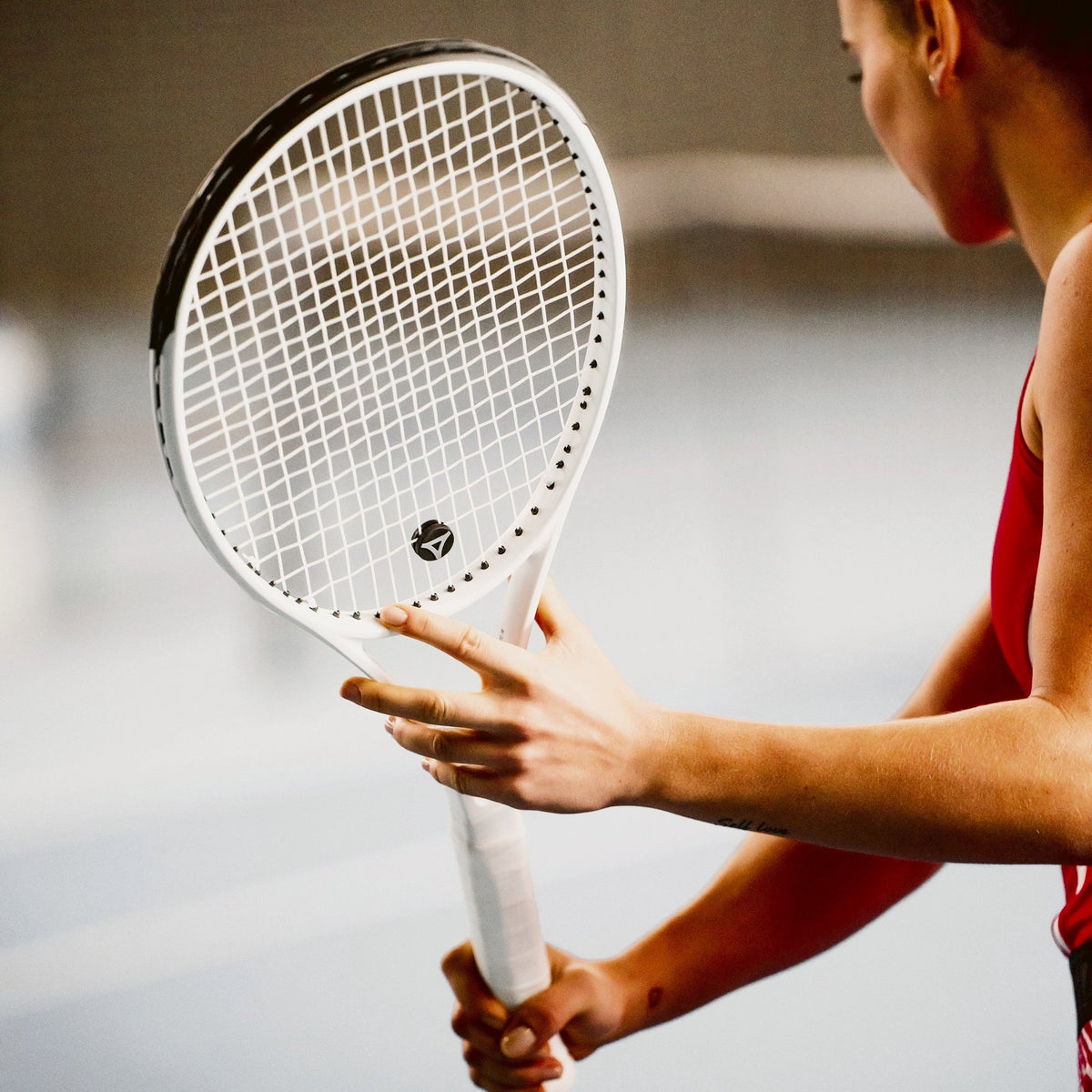 Hráčka kontroluje výpletový vzor a tlmič vibrácií svojej bielej rakety myRacket