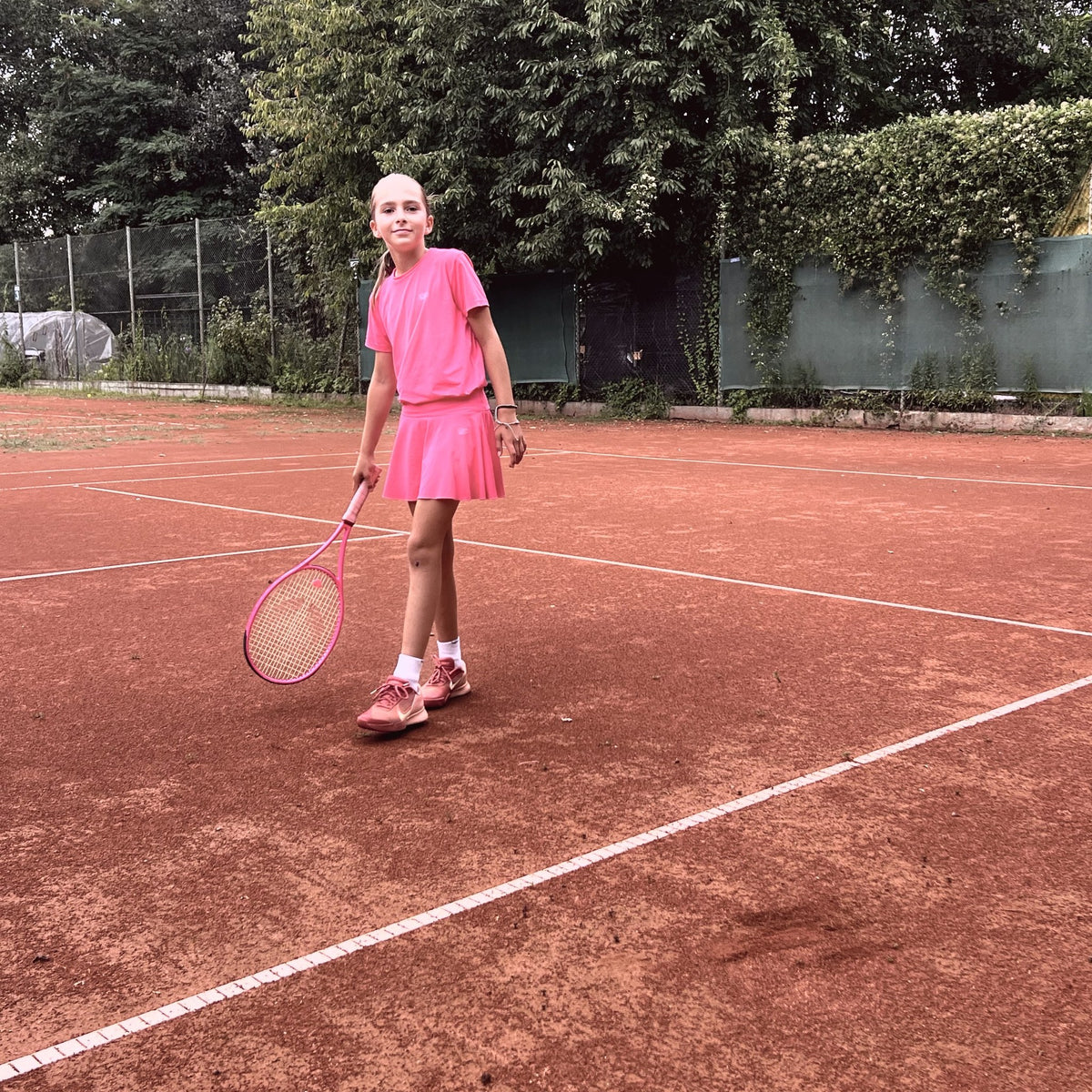 Joven jugadora vestida de rosa con su raqueta junior myRacket en tierra batida