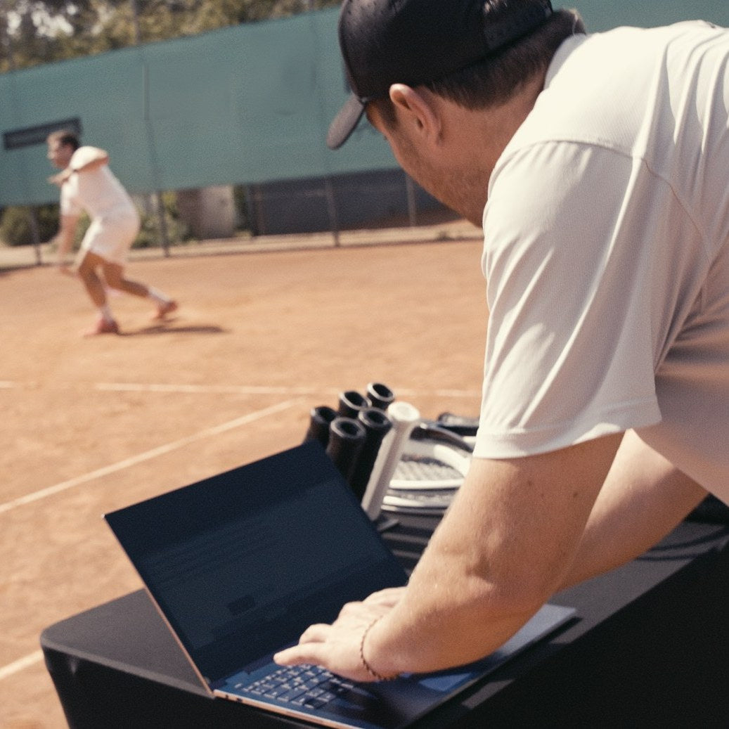 Un fitter analyse sur l'ordinateur portable pendant qu'un joueur essaie des raquettes d'essai sur le court